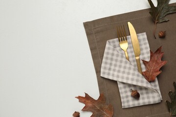 Cutlery, napkin and dry leaves on white background, flat lay with space for text. Table setting