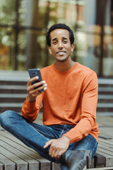 Handsome African American man holding mobile phone, checking mail looking at camera