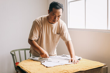Asian man ironing shirt on ironing board at home