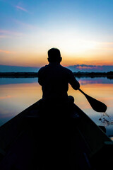 Silhouette of a man paddling canoe at dusk calm water
