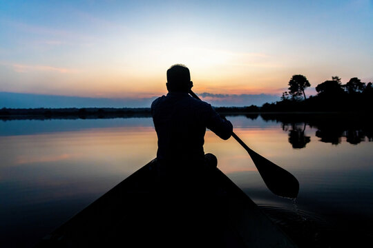 Silhouette of a man paddling canoe at dusk calm water