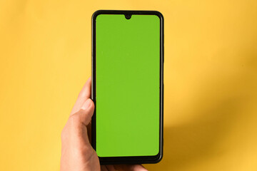 hand holding modern mobile phone green screen isolated on yellow background