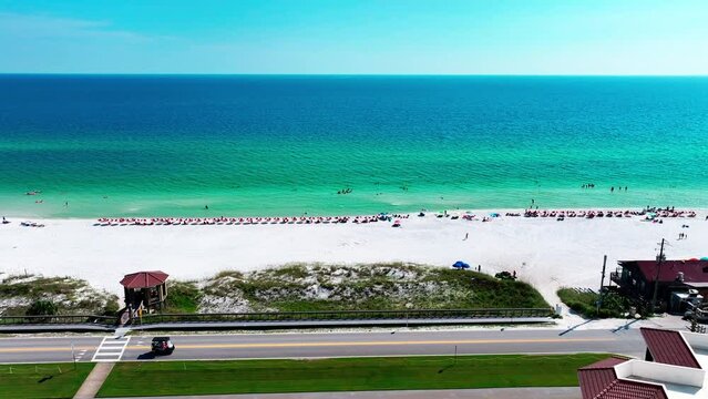 Destin Florida aerial shot flying sideways down old highway 98 with beautiful views of the Gulf of Mexico, white sand, pompano joes restaurant, golf cart, parking lot, beach chairs, and umbrellas.