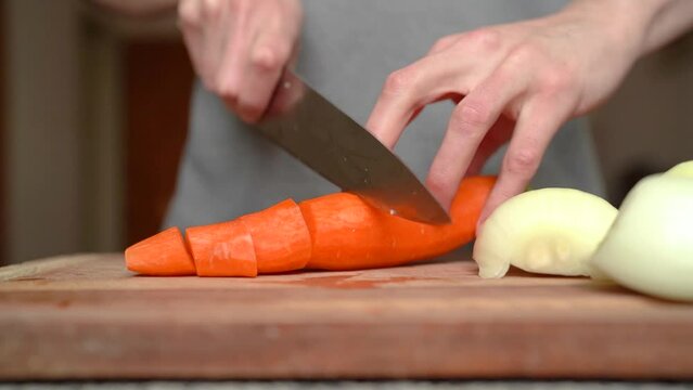 Clean carrot being sliced on wooden cutting board, white onions next