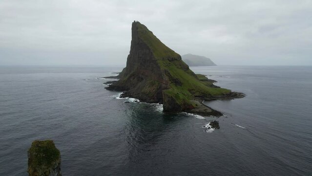 Aerial backwards shot from Tindholmur revealing Drangarnir at the Atlantic Ocean with seagulls flying around
