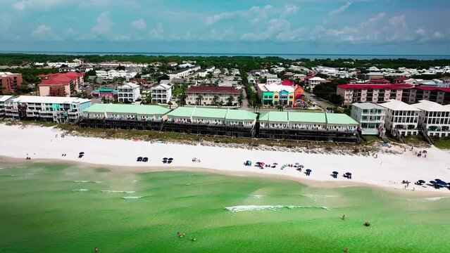 Destin FL aerial shot flying sideways over the Gulf of Mexico with a view of the white sand, emerald green water, pompano joes restaurant, golf cart, parking lot, beach chairs, and umbrellas 1 of 2