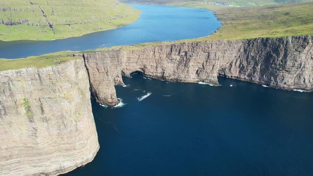 Aerial shot of Lake Sorvagsvatn meander and Traelanipa cliff with hikers on its edge. Faroese landscape