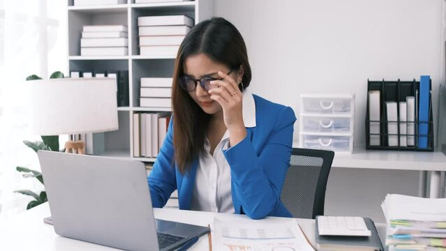 A stressed Asian businesswoman sits at her desk with a serious and unhappy face, upset with her life, worried about her project, and tired of overwork.