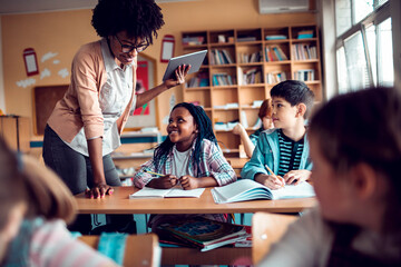 Young African American teacher looking at the work of her students in a elementary school classroom