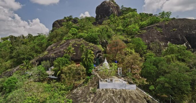 Algama Len Viharaya Sri Lanka Aerial v4 low flyover ancient Buddhist temple perched on the hillside towards the rock mountaintop capturing jungle bush environment - Shot with Mavic 3 Cine - April 2023