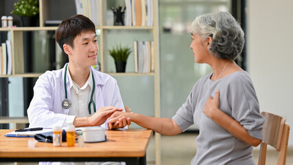 Obraz premium A professional Asian male doctor is talking with an old lady patient in an examination room.