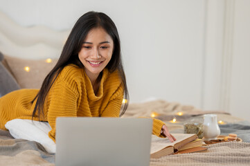 An attractive young Asian female college student is doing homework on her bed in her bedroom.