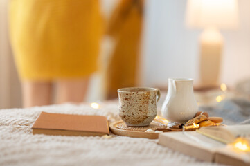 Close-up image of a cup of hot cocoa or coffee, books and decor on a comfy bed in the bedroom.