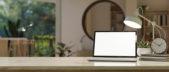 A white screen laptop mockup, a table lamp, accessories, and copy space on a table in a modern room.