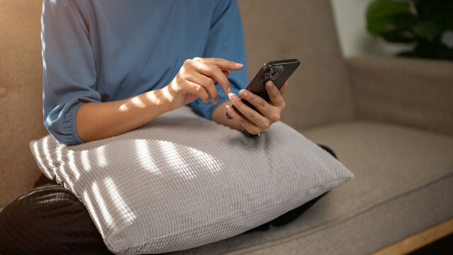 Close-up image of a woman using her smartphone while relaxing on a couch in her living room.