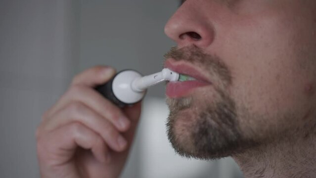 Close-up of man cleaning teeth by an ultrasonic toothbrush. Male brushing his teeth with electric teethbrush. Theme oral health and dental hygiene. Morning sanitation procedures in the bathroom. 