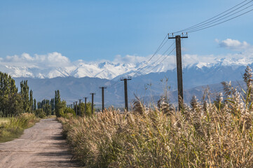 Rural road in a mountain valley and power line against the backdrop of snow-capped mountains....