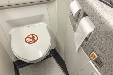 The toilet seat with the lid closed at a aircraft lavatory. With toilet paper on the right.