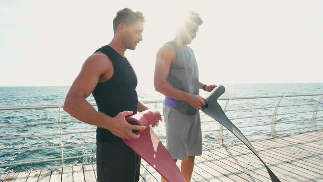 Men discuss workout collecting yoga mats overlooking sea