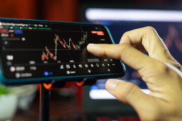 An Investor analysis the stock market exchange from the candlestick graph. Trader at home office trading on computer and using mobile phone. Financial and broker agent investment concept.