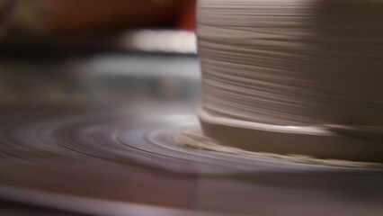 A potter working a clay jug on a potter's wheel with a special tool. A close-up view. A potter is practising pottery, handicraft, working with clay. Slow motion