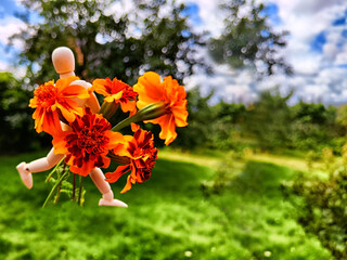 Wooden toy man with flowers against background grass in nature. Concept of holiday, gift bouquet,...