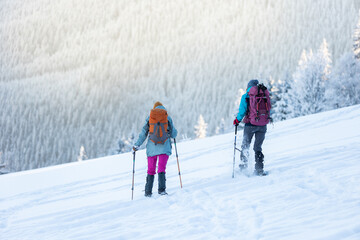 hiking in the mountains on snowshoes. two girls with backpacks go hiking in the snow. Travel and adventure concept.