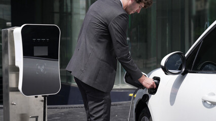 Progressive businessman unplugs charger plug from charging station to his electric car before...