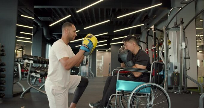 Disabled athlete in wheelchair works out punches with a coach