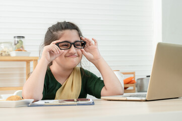 Happy cute little Asian girl wear eyeglasses online learning class, studying with teacher using laptop in kitchen, enjoying online education. Homeschooling, Distance Learning