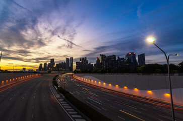 express highway leads to singapore city down town city central district in sunset time, highway bridge with many skyscraper financial buildings in background during rush hour