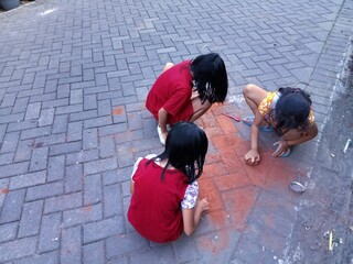 three little asian girl playing brick fragments as chalk for drawing 