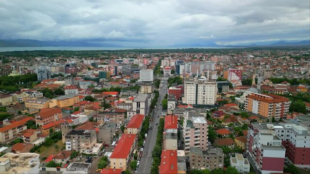 Aerial drone backward moving shot over a main road on both sides of city buildings in Shkodra, also known as Shkoder or Scutari in Albania on a cloudy day