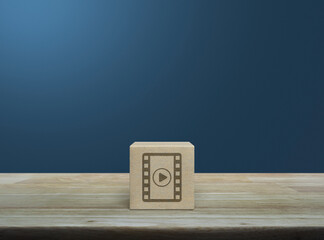 Play button with movie icon on wood block cube on wooden table over light blue wall, Business cinema online concept