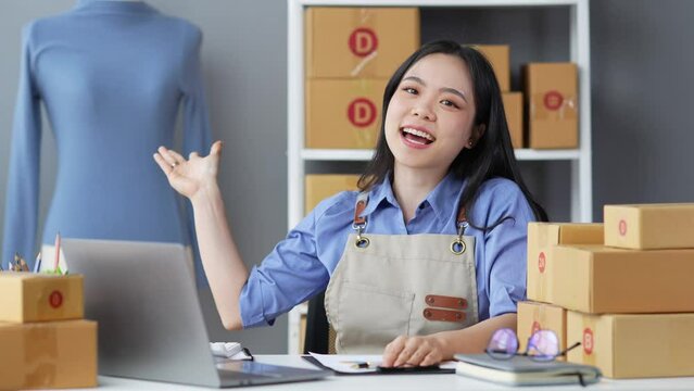 Small business startup images SME business owner, female entrepreneur talking online via laptop to check orders and prepare sales boxes for customers. Online SME business concept.