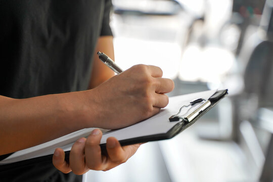 Closeup Asian young officer of the gym and fitness trainer checking fitness equipment maintenance list at fitness center.