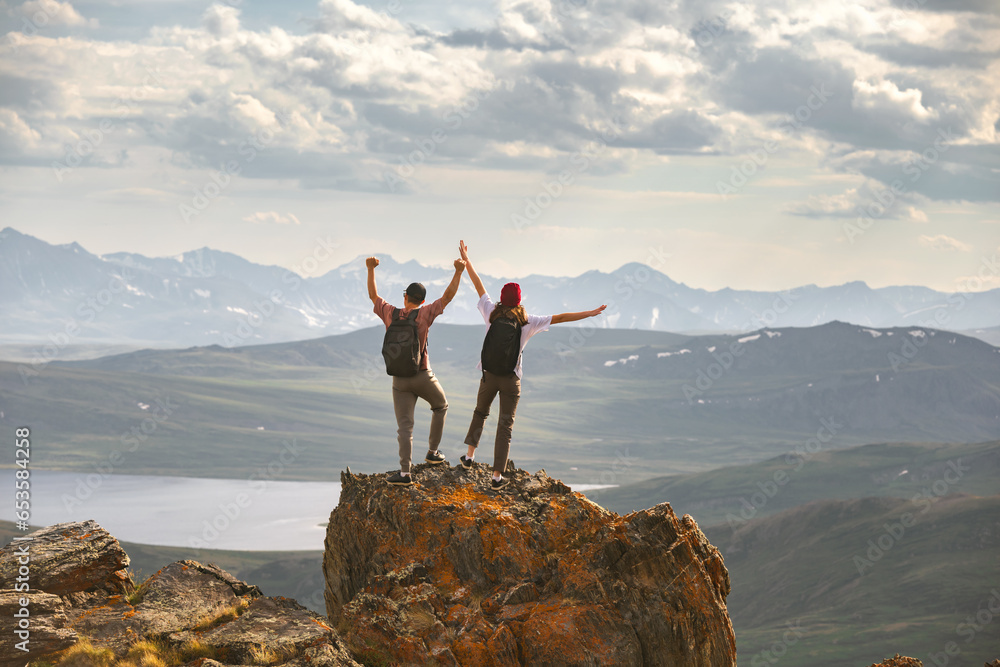 Aufkleber Young couple of hikers with backpacks are standing at mountain top with open arms in winner pose