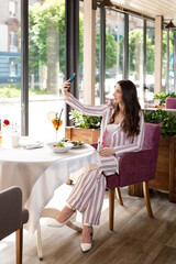 brunette girl has dinner, lunch in a restaurant. eats salad and cocktail, girl waits for friends in restaurant