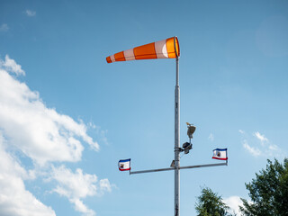 Windscock and flag flutter in the wind on a tall pole. The weather station