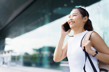 Happy beautiful Asian woman tourist talking on mobile phone while walking at the airport terminal, female passenger talks with friends and family at the airport terminal before boarding.