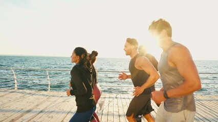 Group of focused athletes jogging along sea at sunset