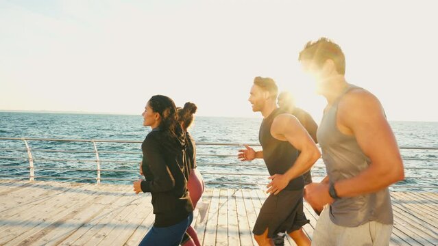 Group of focused athletes jogging along sea at sunset