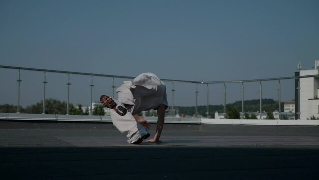 The guy coolly dances breakdance on the roof of the house. Slow motion shooting. A man dances an energetic athletic dance.