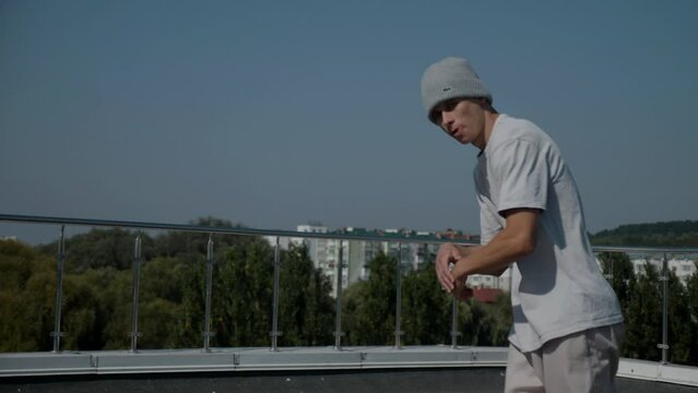The guy coolly dances breakdance on the roof of the house. Slow motion shooting. A man dances an energetic athletic dance.