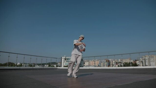 The guy coolly dances breakdance on the roof of the house. Slow motion shooting. A man dances an energetic athletic dance.
