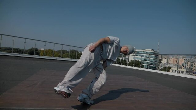 The guy coolly dances breakdance on the roof of the house. Slow motion shooting. A man dances an energetic athletic dance.