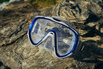 a blue diving mask lies on the rocks near the sea