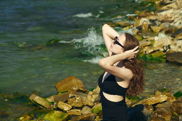 a beautiful woman enjoys a vacation standing near the raging sea and straightens her hair in the wind