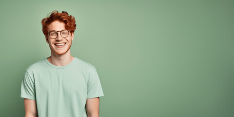 Handsome ginger man wearing green t-shirt and glasses. Isolated on green background.