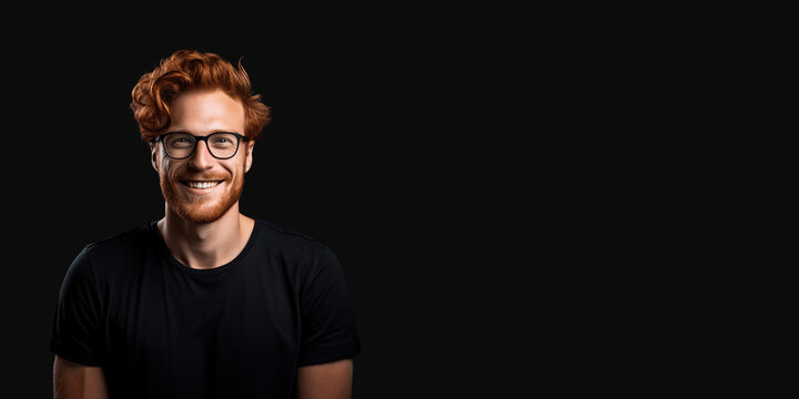 Handsome ginger man wearing black t-shirt and glasses. Isolated on black background.